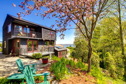 Black wooden modern house with spring backyard and two chairs.