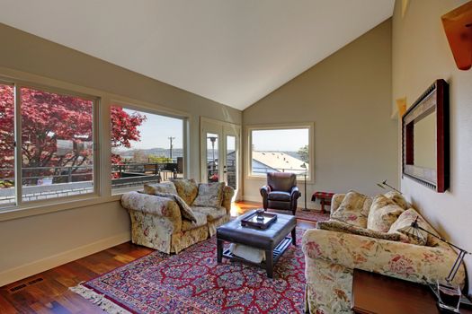 Large living room with two sofas and red rug with many windows.