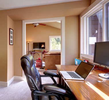 Home office and computer and chair with brown walls and TV in living room.