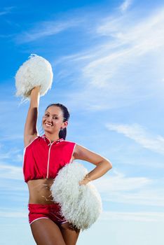 Young cheerleader in red costume with pampon against blue sky