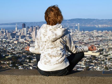  The woman meditates  on a background of Twin Peaks, San Francisco. 