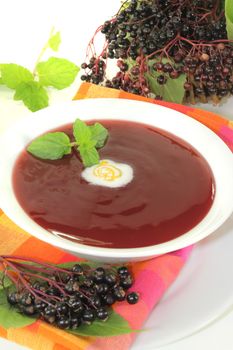 healthy elderberry soup with dollop of whipped cream and mint on a light background