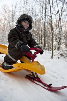 Young boy having fun going dowbhill on a snow sledge