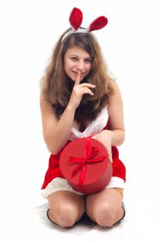 young christmas woman in red santa claus dress with a gift holding finger on lips on white background 