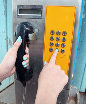 women hand dialing on a public phone