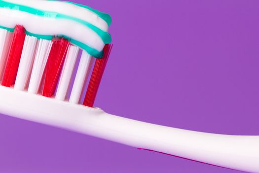 A pink toothbrush with toothpaste on a purple background