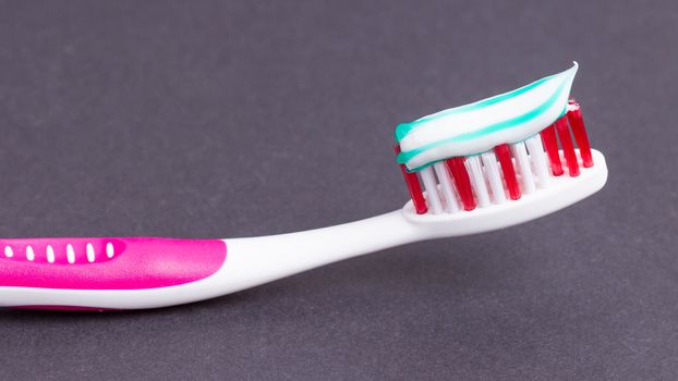 A pink toothbrush with toothpaste on a grey background