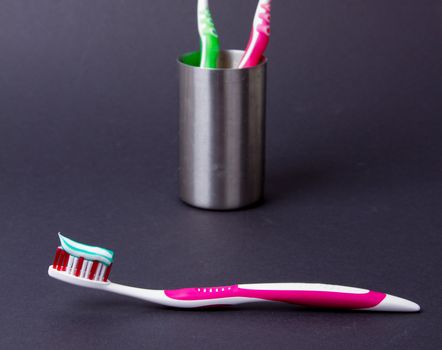 A pink toothbrush with toothpaste on a grey background