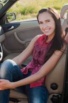 Smiling brunette woman with long hair sitting in car