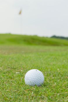 Golf ball on grass above flag and green course