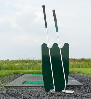 Two golf clubs standing at a driving range