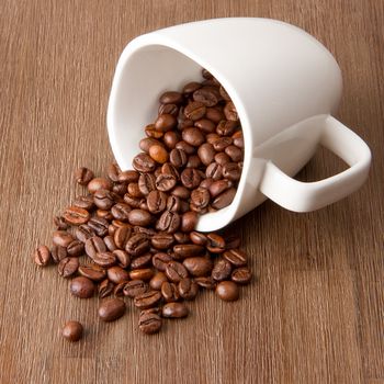 Coffee cup and spilled coffee beans on wood