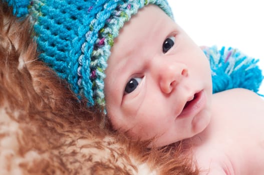 Shot of newborn baby in blue hat lying on fur