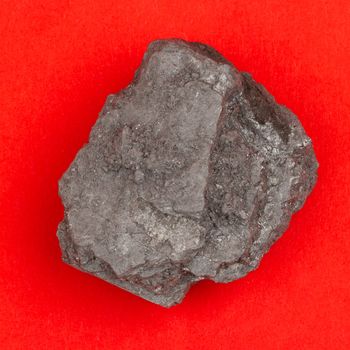Rough specimen of black coal, a combustible sedimentary rock on a red background