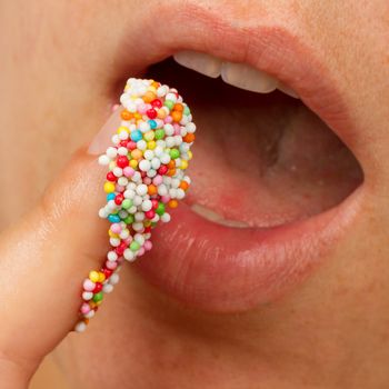 Close-up of woman lips and finger with multicolored pearls