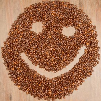 Coffee grains arranged in smiley. Isolated on wooden background.