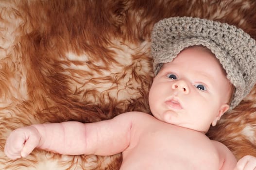 Cute newborn baby in hat lying on fur