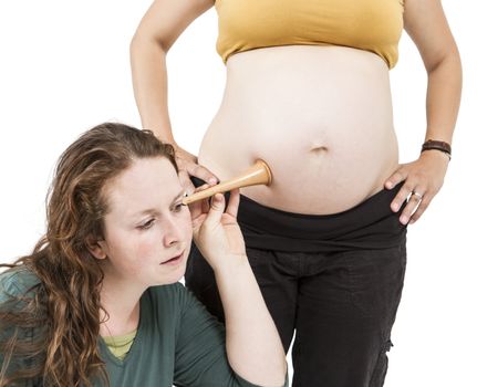 young midwife listening at human belly. pregnant woman standing while midwife is sitting in front. horizontal picture isolated on white