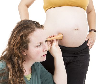 young midwife listening at human belly. pregnant woman standing while midwife is sitting in front. horizontal picture isolated on white