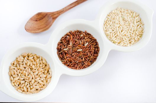  rice , red rice , wheat  grains on white bowl and wooden spoon