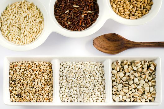 rice , red rice , wheat,  job's tears , barley and millet grains on white bowl , top views of grain and wooden spoon ,  