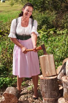 Bavarian farmer with Dirndl chopping wood