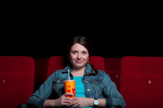 beautiful woman in a movie theater, watching a movie and drink a drink