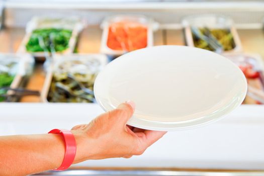 Hand wearing all-inclusive bracelet holding empty plate against vegetarian buffet table