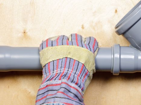 Plumber's hand wearing protective glove with pvc sewage pipes