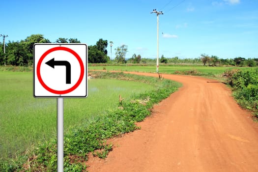 Turn left sign with soil road in countryside