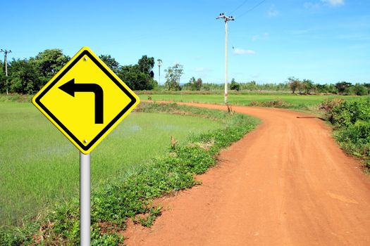 Turn left warning sign with soil road in countryside