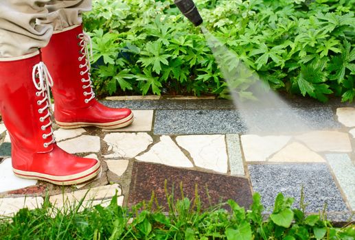 Person in red gumboots cleaning garden alley with a pressure washer