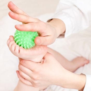 Masseur massaging child's foot with rubber device, shallow focus
