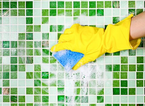 Hand in yellow protective glove cleaning mosaic wall