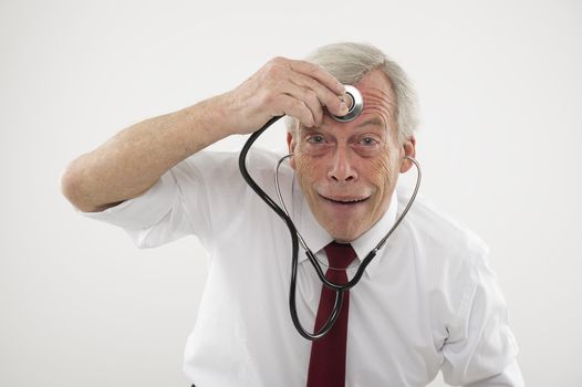 Humorous medical concept of a senior man pulling a comical face holding a stethosope to his forehead as though checking his brain function, intellect, wisdom or cognitive powers