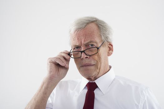 Handsome retired man in glasses peering over the top of the frames at the camera with a frown, head and shoulders studio portrait