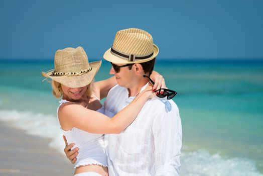 Romantic embracing young couple in hats and white dress on a tropical blue sea 