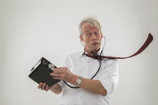 Conceptual studio shot over white of an old man with a hearing problem, who is using a stethoscope to try and hear his audio speakers