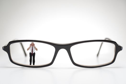 Diminutive elderly man peering through a lens on a pair of spectacles or prescription glasses , a humorous take on aging eyesight requiring corrective glasses