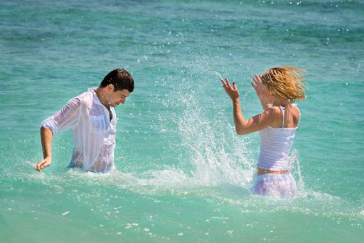 Playful young couple have a fun in blue sea water on the tropical beach 