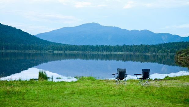 Two foldable camping chair on a mountain lake shoreline in the evening