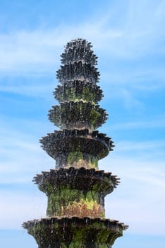 Big old fountain covered by green moss with blue cloudy sky on background