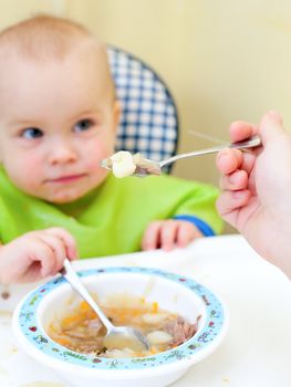 Mother feeding little baby girl in a highchair, focus on spoon with food