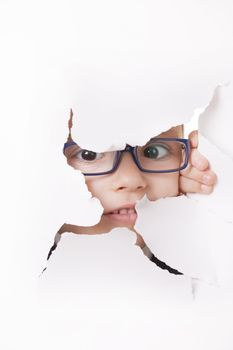 Curious kid in spectacles looks through a hole in white paper