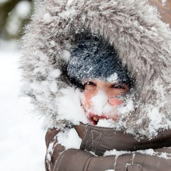 Young boy wearing winter jacket with furry hood playing in snow