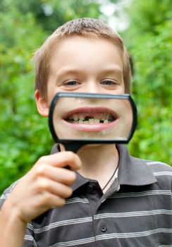 Young boy showing missing baby tooth through hand magnifier, shallow DOF