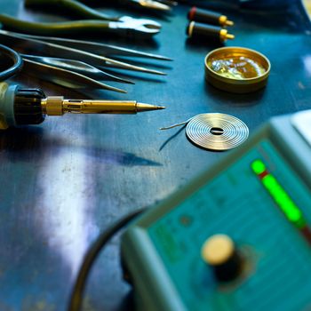 Soldering station with soft solder and tools in background, shallow DOF