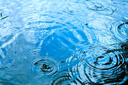 Rain drops rippling in a puddle with blue sky reflection