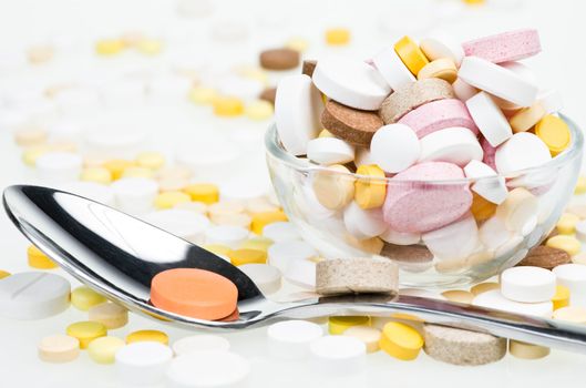 Spoon with orange tablet near glass bowl overfilled with tablets