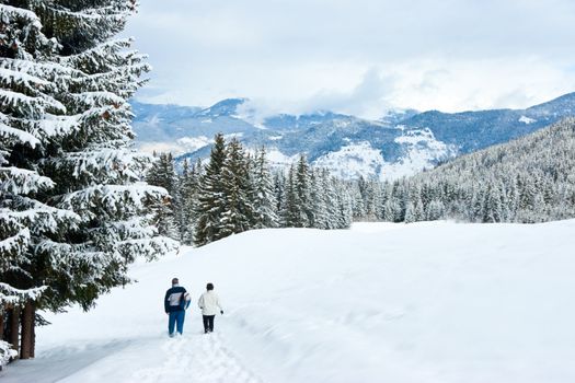 Two hikers in snowy winter forest at French Alps